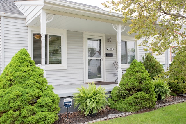 entrance to property featuring a porch and roof with shingles