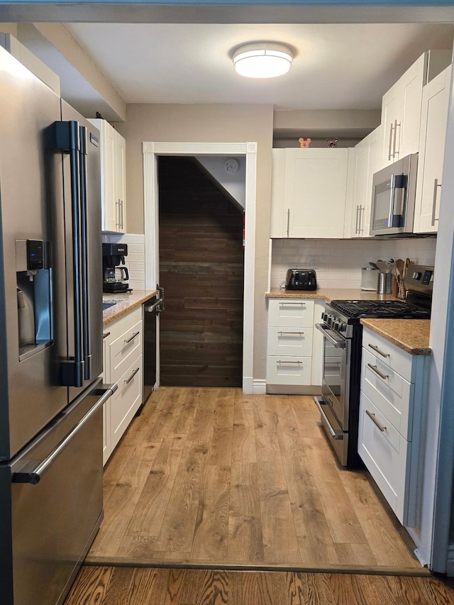 kitchen with stainless steel appliances, white cabinets, light stone countertops, backsplash, and light wood-style floors