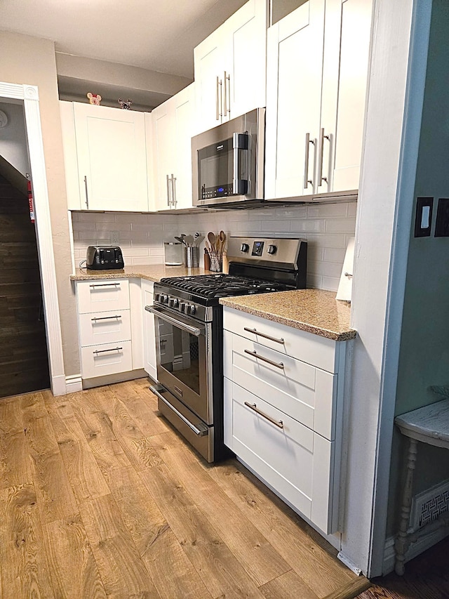 kitchen featuring stainless steel appliances, tasteful backsplash, white cabinetry, light stone countertops, and light wood-style floors
