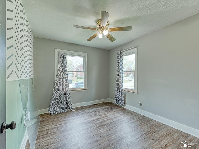 spare room featuring a textured ceiling, baseboards, a wealth of natural light, and wood finished floors