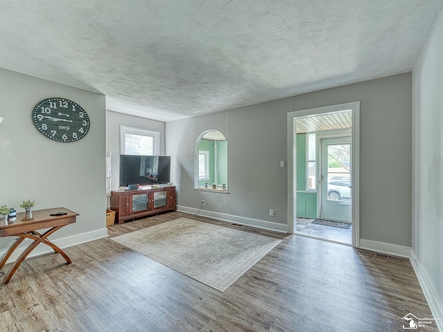 unfurnished living room with baseboards, plenty of natural light, a textured ceiling, and wood finished floors