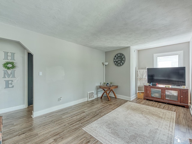 living room with a textured ceiling, baseboards, and wood finished floors