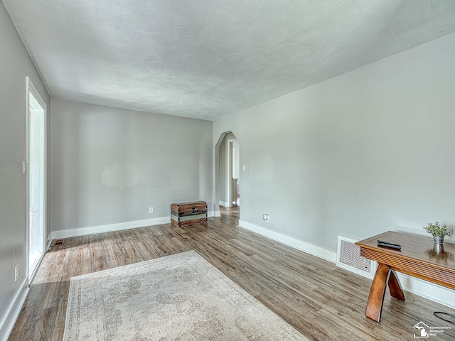 unfurnished living room with baseboards, arched walkways, wood finished floors, and visible vents