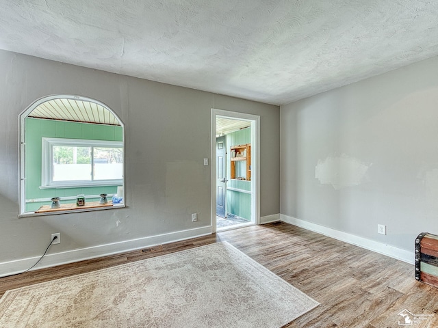 spare room featuring baseboards, a textured ceiling, and wood finished floors