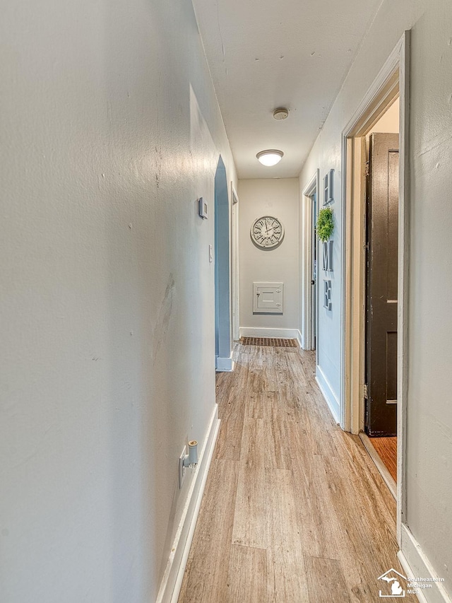 hallway featuring arched walkways, baseboards, and light wood-type flooring