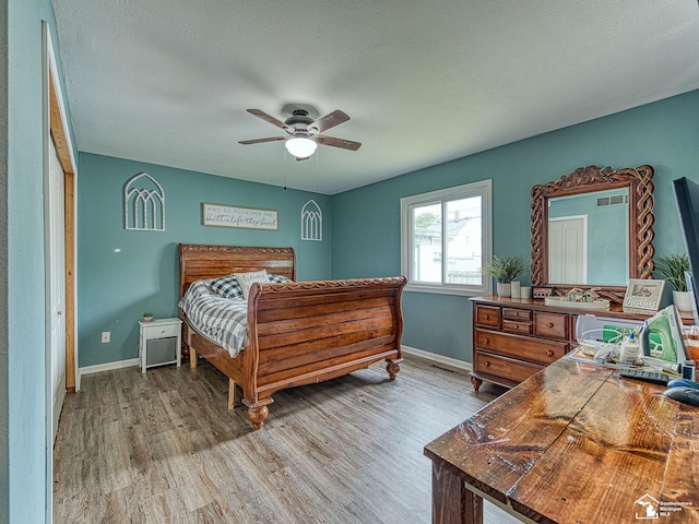 bedroom featuring a ceiling fan, baseboards, light wood-style flooring, and a textured ceiling