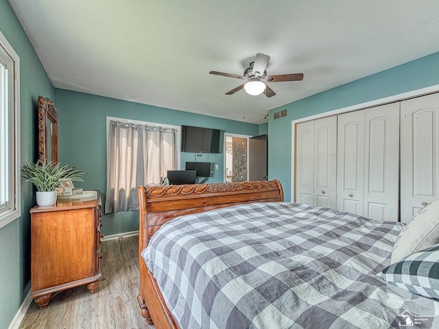 bedroom featuring a closet, visible vents, wood finished floors, baseboards, and a ceiling fan