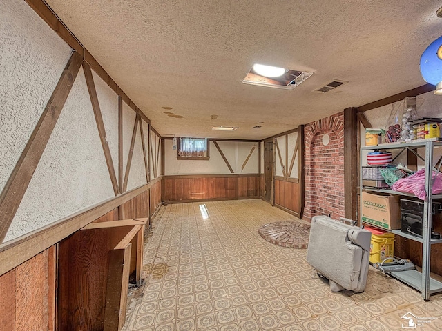 interior space with a textured ceiling, visible vents, wood walls, and a wainscoted wall