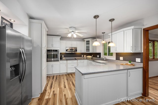 kitchen with a peninsula, a sink, stainless steel appliances, white cabinetry, and light wood-type flooring