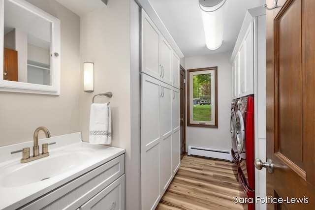 clothes washing area with baseboard heating, light wood finished floors, a sink, separate washer and dryer, and cabinet space
