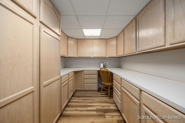 kitchen featuring built in desk, light wood-type flooring, light countertops, a drop ceiling, and light brown cabinets