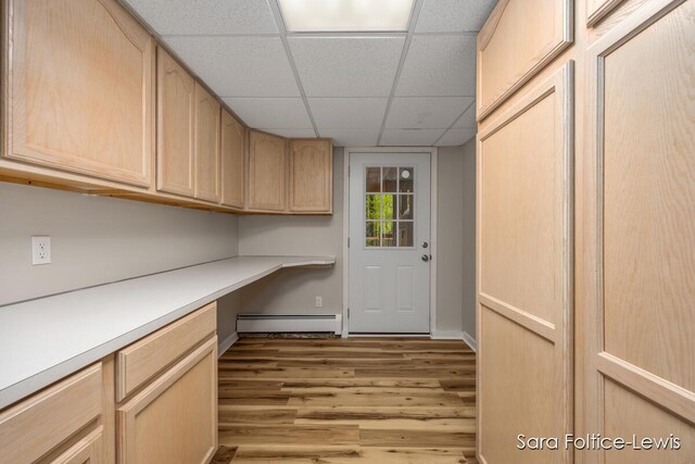 unfurnished office with built in study area, wood finished floors, baseboard heating, a drop ceiling, and baseboards