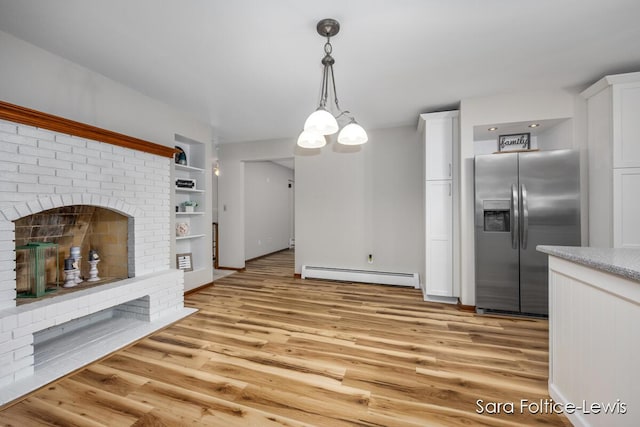 kitchen featuring pendant lighting, a baseboard radiator, light wood finished floors, stainless steel fridge, and white cabinets