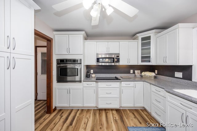 kitchen with appliances with stainless steel finishes, a ceiling fan, glass insert cabinets, white cabinets, and light wood-style floors