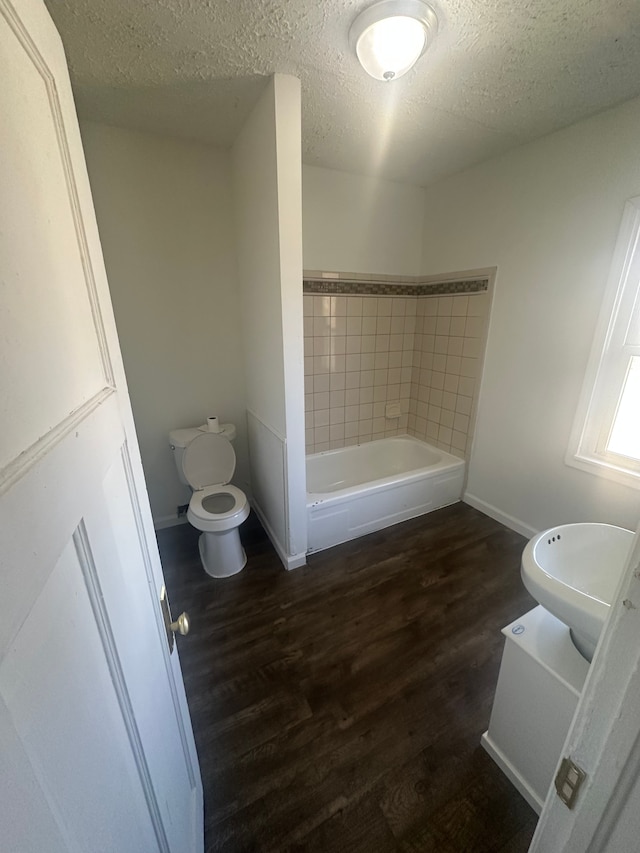 bathroom with a bathtub, toilet, wood finished floors, and a textured ceiling