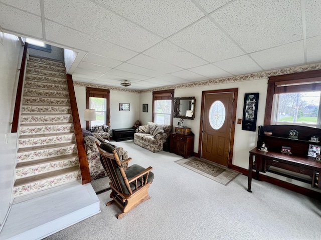 living area featuring baseboards, carpet, a paneled ceiling, and stairway