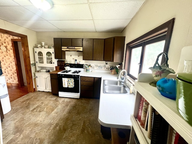 kitchen with a paneled ceiling, a sink, light countertops, under cabinet range hood, and gas range oven
