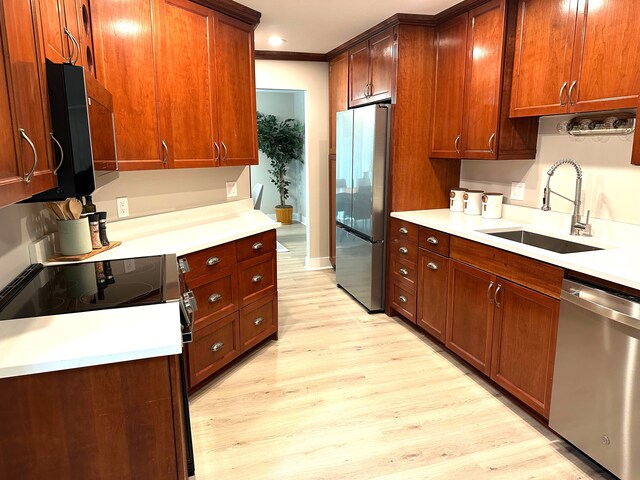 kitchen featuring appliances with stainless steel finishes, a sink, light wood-type flooring, light countertops, and crown molding