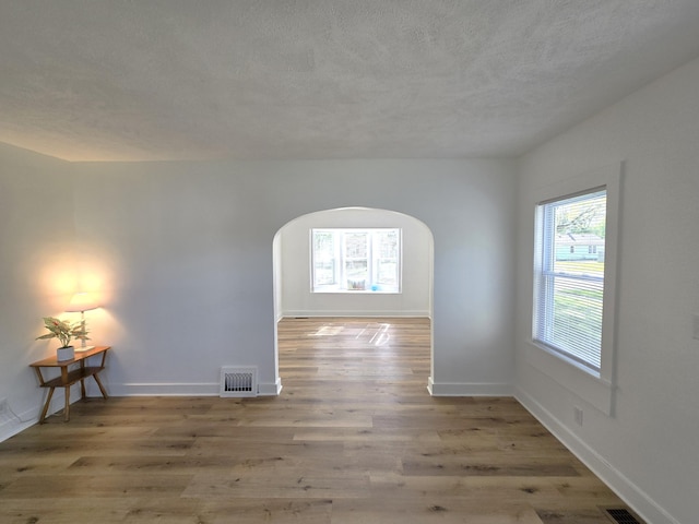 unfurnished room with a textured ceiling, visible vents, arched walkways, wood finished floors, and baseboards