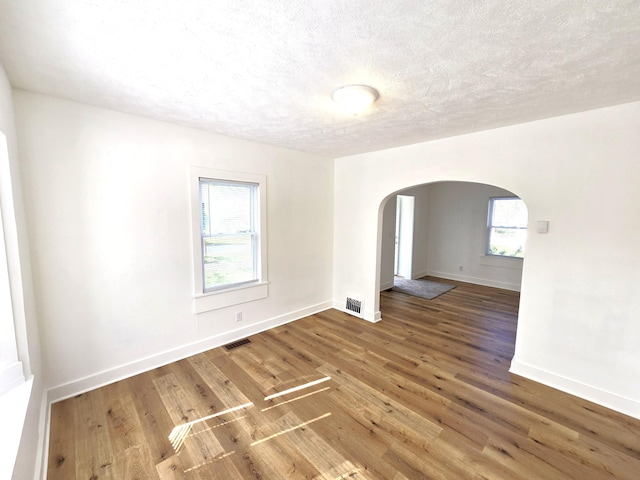 spare room featuring arched walkways, baseboards, visible vents, and wood finished floors