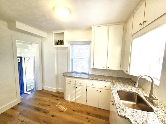 kitchen with tasteful backsplash, a sink, baseboards, light wood-style floors, and white cabinetry