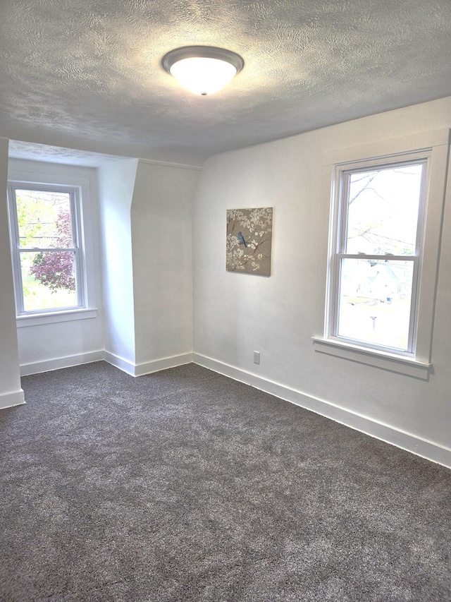 unfurnished room featuring dark colored carpet, a textured ceiling, and baseboards