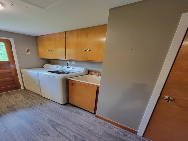 laundry area featuring cabinet space, washer and dryer, a sink, and light wood-style floors