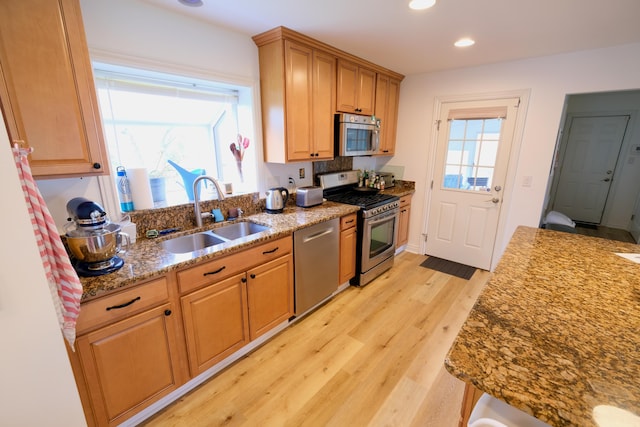 kitchen with appliances with stainless steel finishes, light stone counters, a sink, light wood finished floors, and plenty of natural light