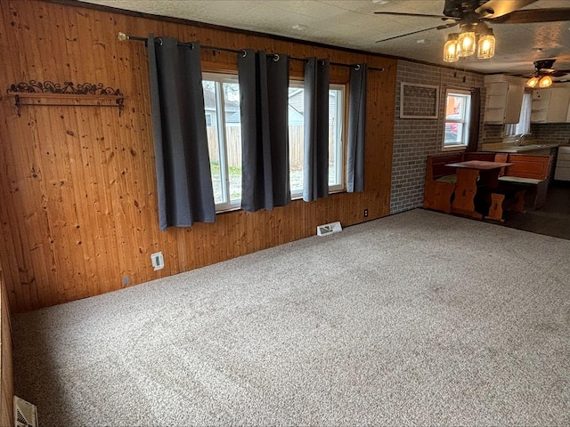 interior space with wooden walls, a ceiling fan, visible vents, and carpet floors
