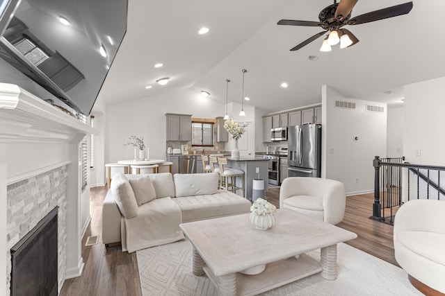 living room featuring a fireplace, vaulted ceiling, a ceiling fan, and visible vents