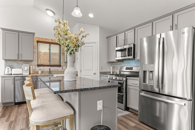 kitchen featuring dark stone countertops, gray cabinets, vaulted ceiling, backsplash, and appliances with stainless steel finishes