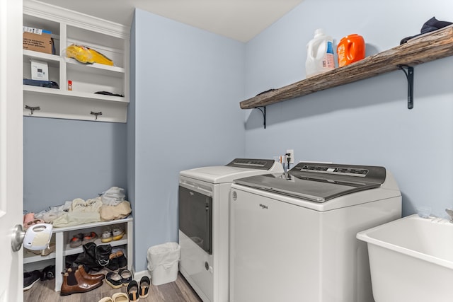 clothes washing area with washing machine and clothes dryer, laundry area, a sink, and wood finished floors