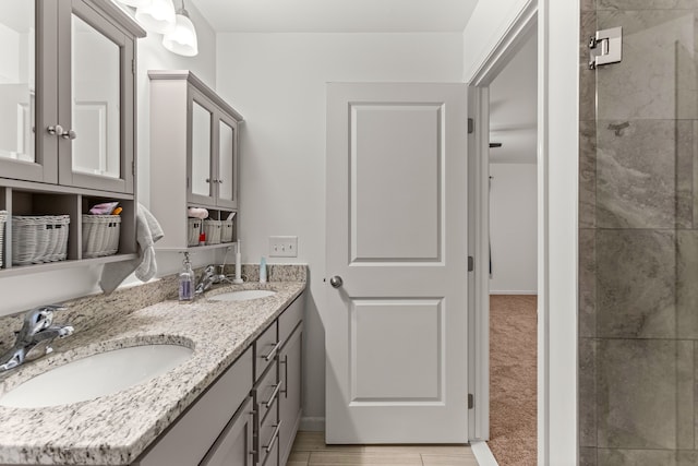 bathroom featuring baseboards, a tile shower, double vanity, and a sink