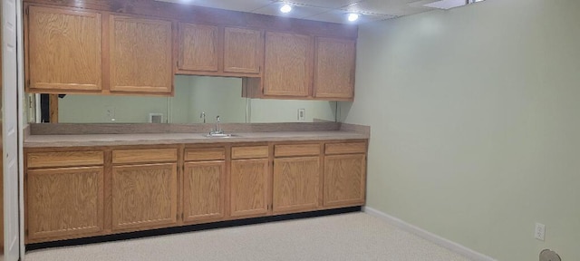 kitchen featuring light countertops, baseboards, a sink, and light colored carpet