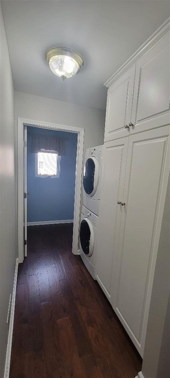 clothes washing area featuring dark wood-style flooring, laundry area, stacked washing maching and dryer, and baseboards