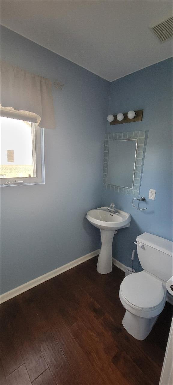 half bath featuring baseboards, toilet, wood finished floors, and visible vents