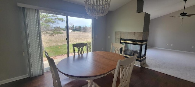 dining space featuring dark wood-style flooring, baseboards, a tile fireplace, ceiling fan with notable chandelier, and vaulted ceiling