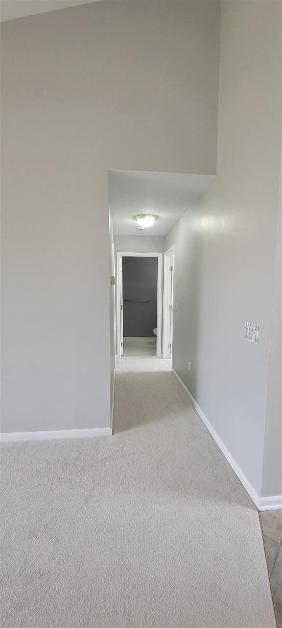 hallway with baseboards and light colored carpet