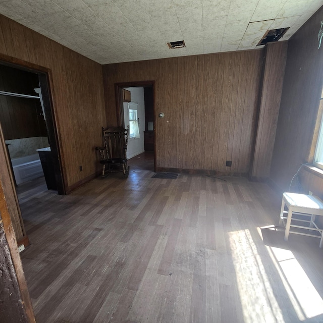 unfurnished room with wooden walls, wood finished floors, and visible vents