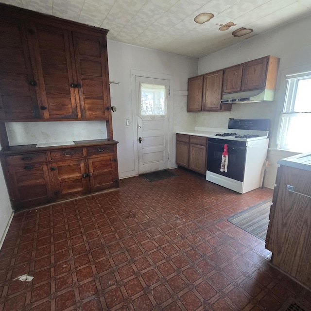 kitchen featuring under cabinet range hood, dark floors, gas range gas stove, and light countertops