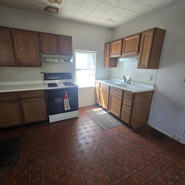 kitchen featuring range with gas cooktop, brown cabinets, a sink, light countertops, and under cabinet range hood