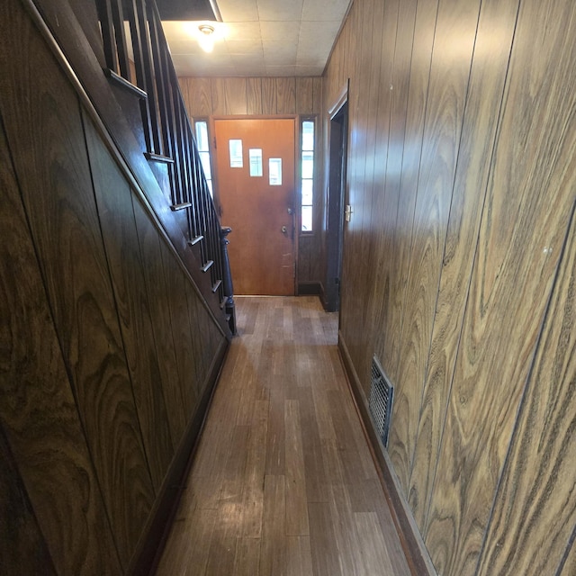 corridor with wooden walls, stairway, dark wood finished floors, and visible vents