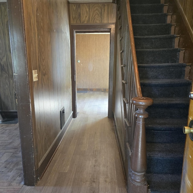 staircase with wooden walls, baseboards, wood finished floors, and visible vents