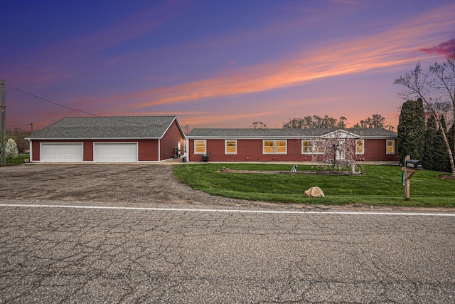 ranch-style house featuring a garage, an outbuilding, a lawn, and aphalt driveway