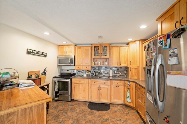 kitchen with backsplash, a sink, glass insert cabinets, stainless steel appliances, and recessed lighting