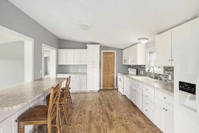 kitchen with a sink, white appliances, a kitchen breakfast bar, wood finished floors, and vaulted ceiling
