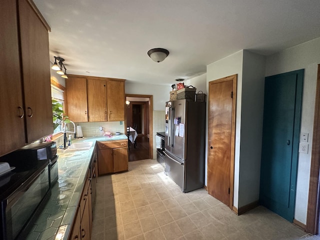 kitchen with a sink, brown cabinetry, freestanding refrigerator, tile countertops, and backsplash