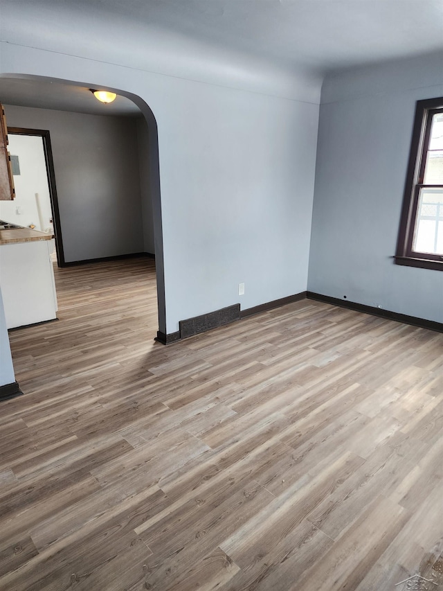 unfurnished room with arched walkways, baseboards, and wood finished floors