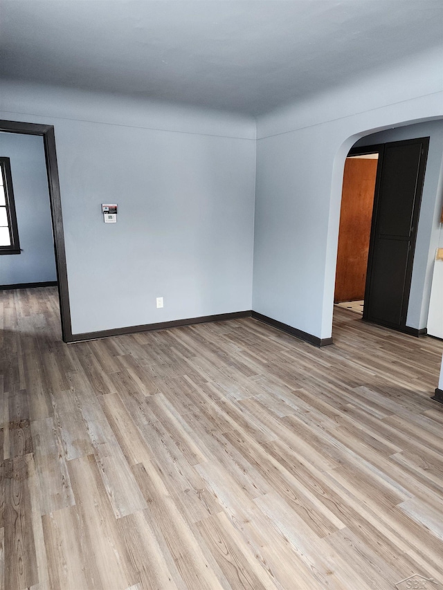 unfurnished room featuring arched walkways, baseboards, and light wood-type flooring