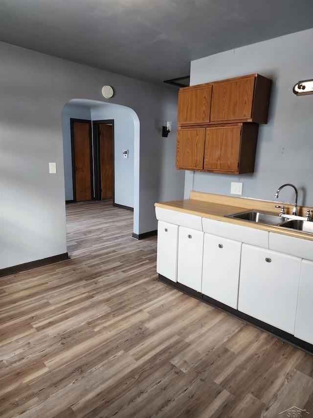kitchen with baseboards, a sink, light wood finished floors, and arched walkways